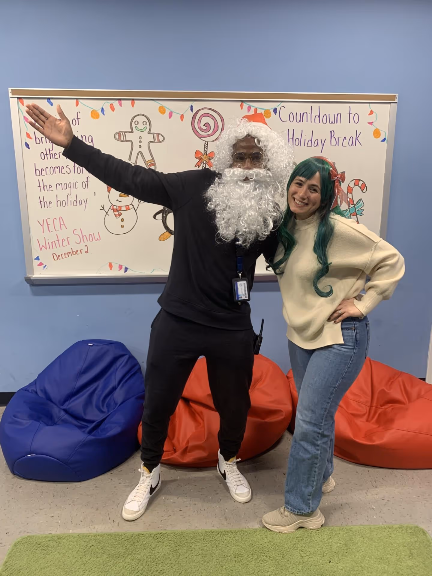 Two people in costume posing playfully in front of a classroom wall