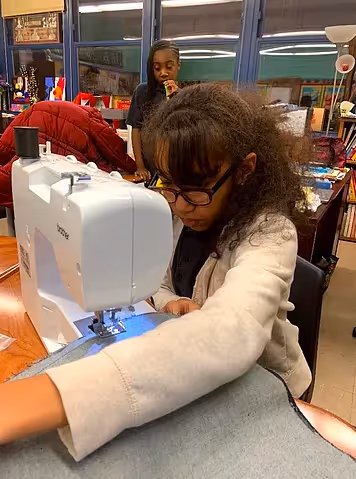 Girl sewing with a sewing machine in a classroom.