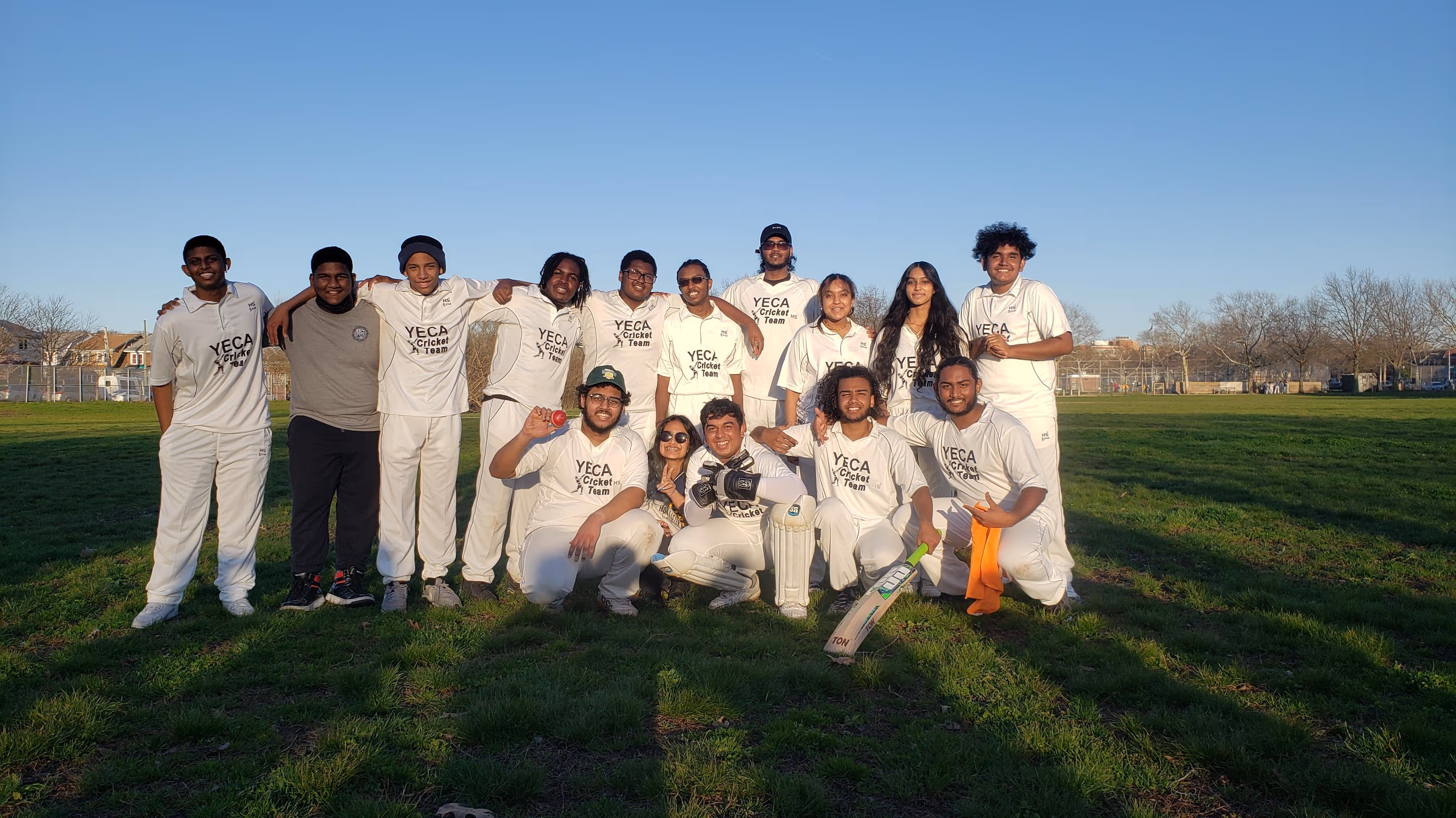Group of students in white uniforms posing for a team photo on a grassy field.
