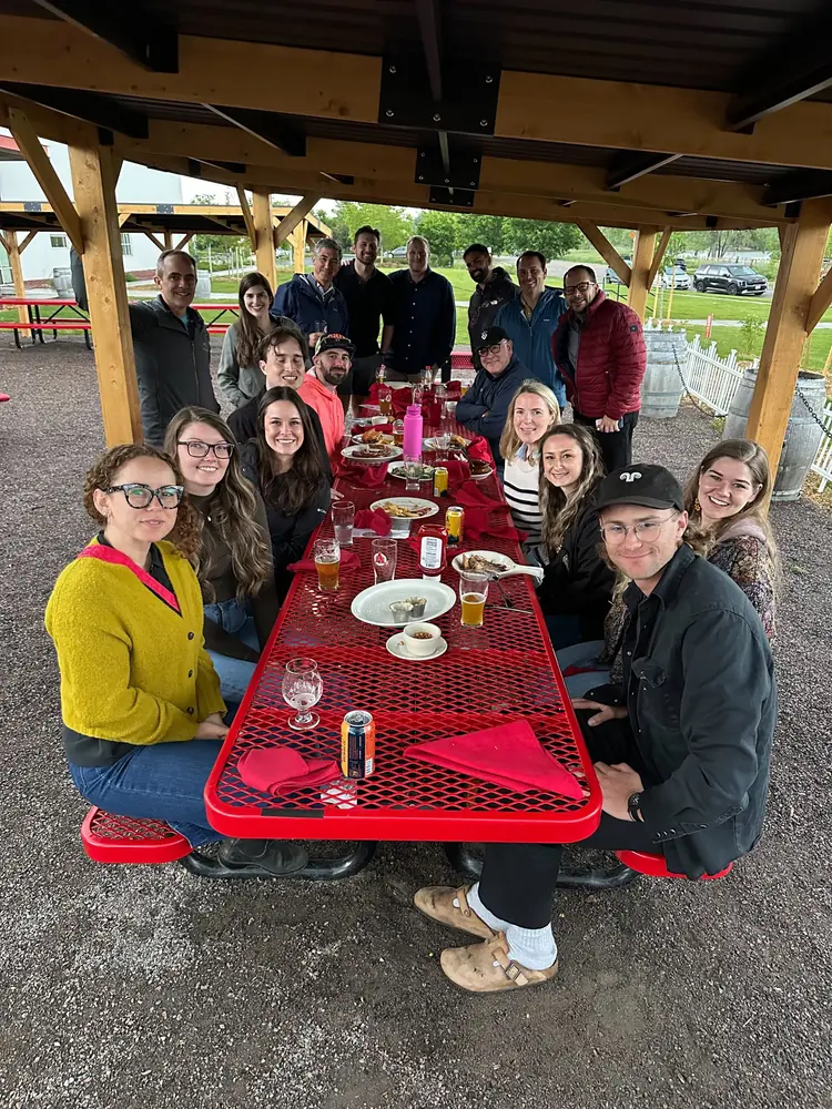 The team sharing dinner at a long picnic table under an outdoor pavilion