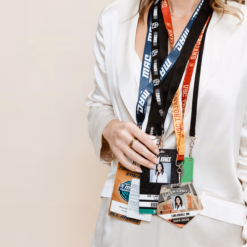 Person wearing a white jacket holding multiple lanyards with ID badges including one labeled 'Dr. Lara Oberle, MD' and another with 'USC Trojans' text.