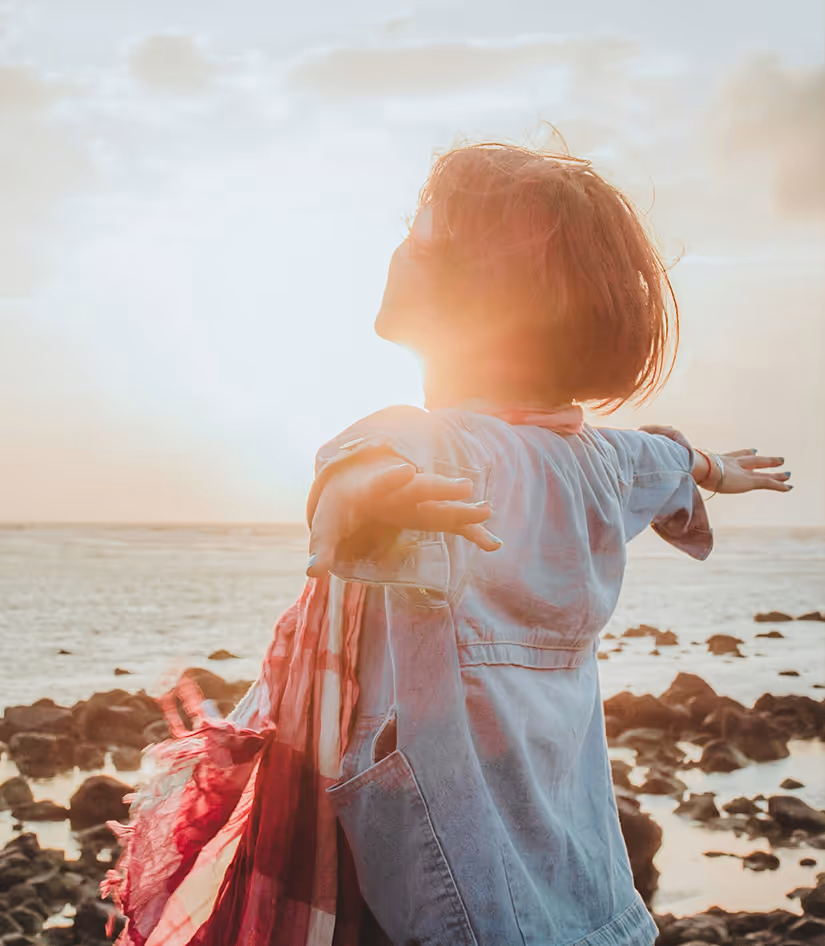 «Ένα άτομο με ανοιχτές τις αγκάλες σε μια παραλία την ώρα του ηλιοβασιλέματος, εκφράζοντας ελευθερία, χαρά και προσωπική ανάπτυξη.»