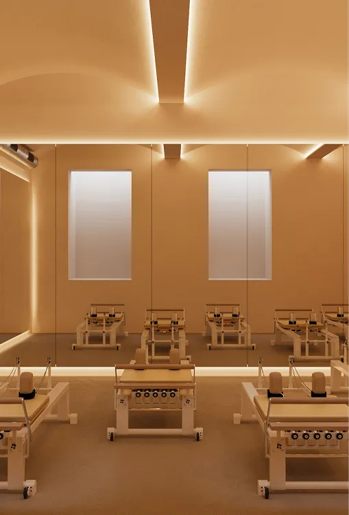 Minimalist Pilates studio with wooden reformer machines, large mirrors, and soft ambient lighting.