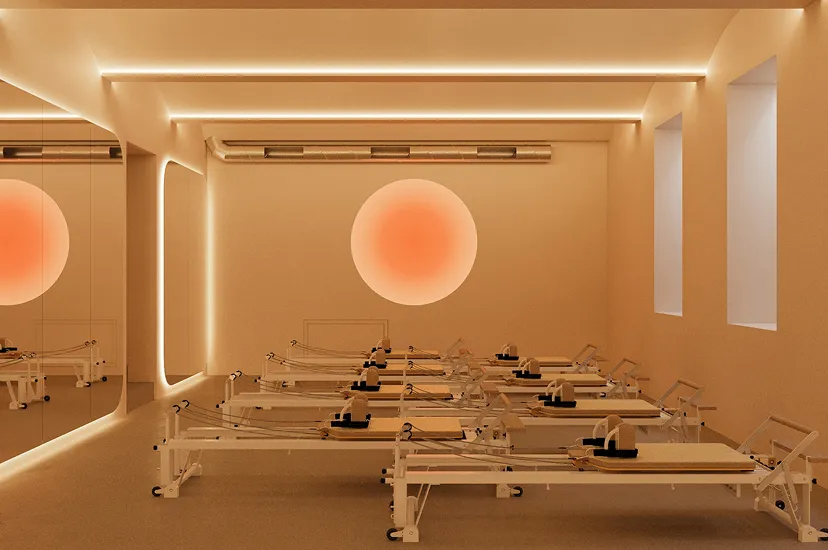 Modern Pilates studio with multiple reformer machines arranged in rows under soft warm lighting and a glowing circular wall light.
