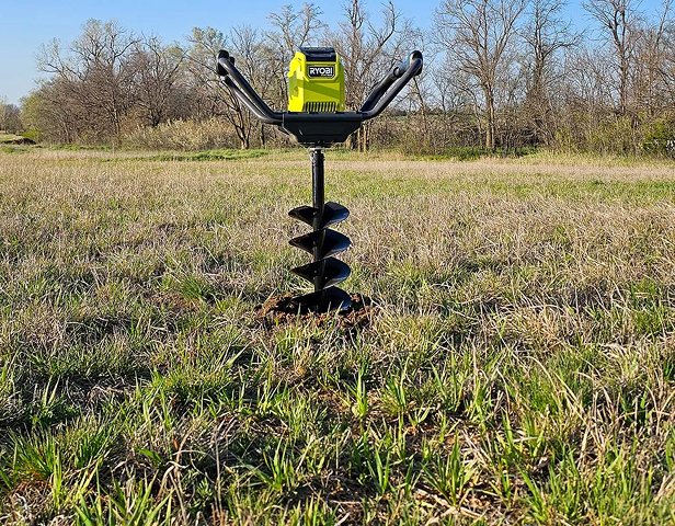 A professional and electric auger halfway in the ground and upright.