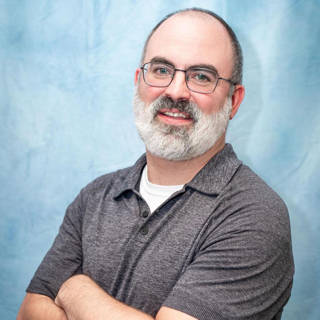 Professional headshot of staff member with gray beard and glasses