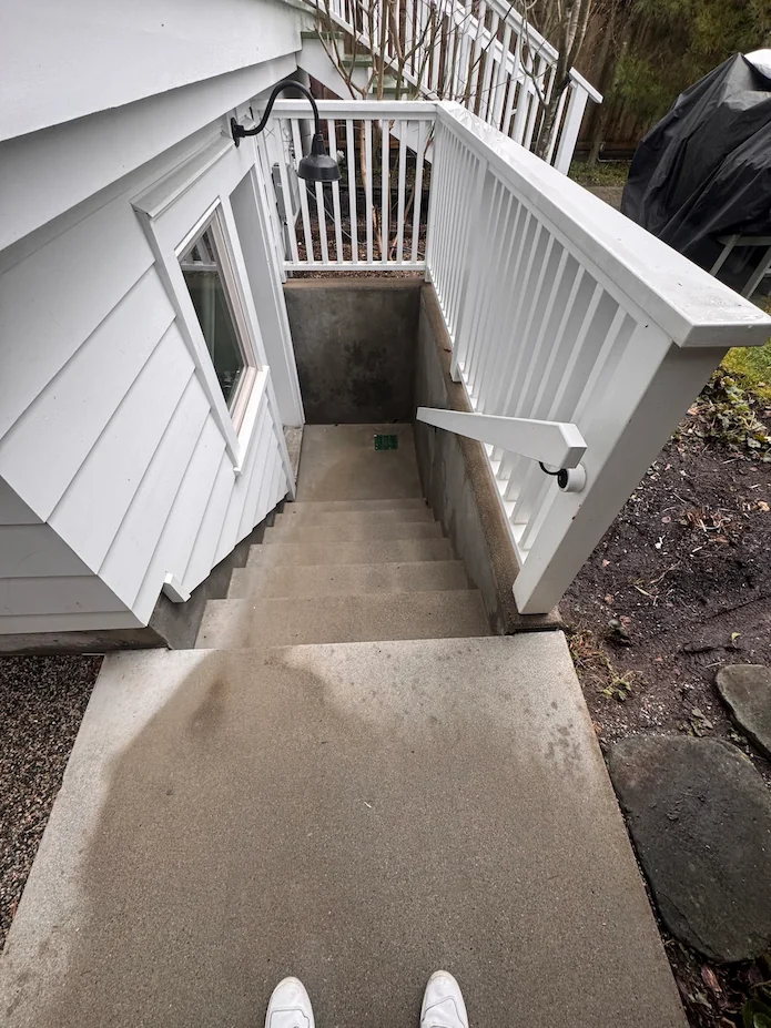 Clean concrete basement stairwell after professional pressure washing, showing bright steps and white railing.