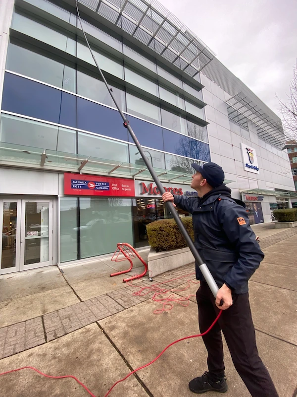 Professional window cleaner using a water-fed pole system to clean exterior windows of a commercial office building.