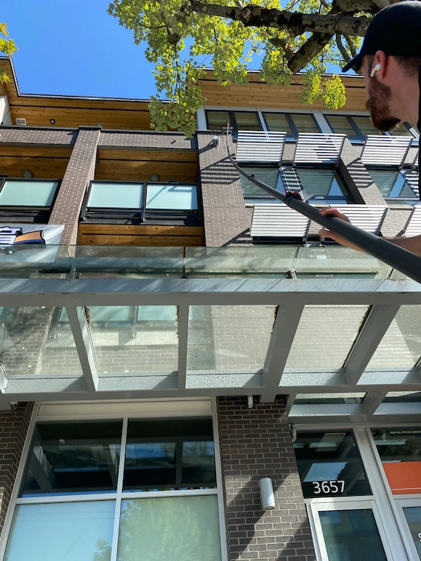 Window cleaner using an extension pole to wash glass exterior of a commercial building in bright daylight.