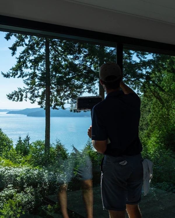 Professional cleaner washing large interior windows with ocean view in Lions Bay home.