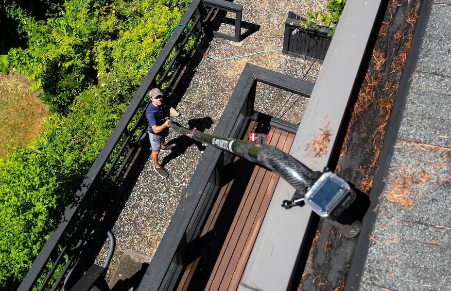 Top-down view of technician performing gutter cleaning on residential home using extension pole.