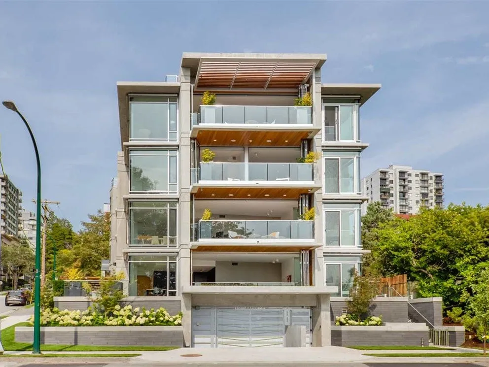 Modern four-story condominium building with large glass balconies and landscaped greenery in front.