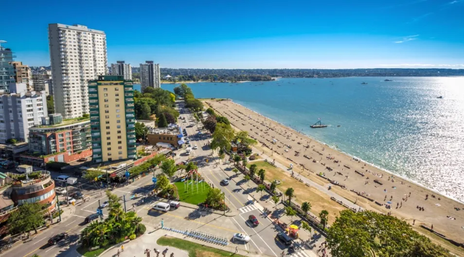 A sunny urban beach scene with high-rise buildings, a sandy beach filled with people, and a sparkling blue ocean under a clear sky.