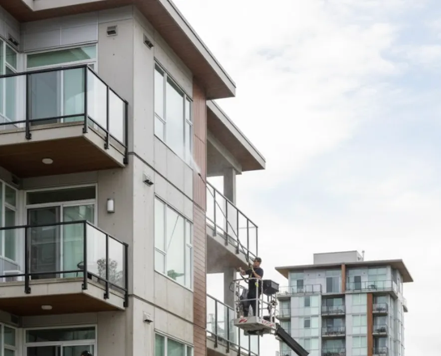 Worker on a lift power washing the exterior balconies of a modern apartment building.
