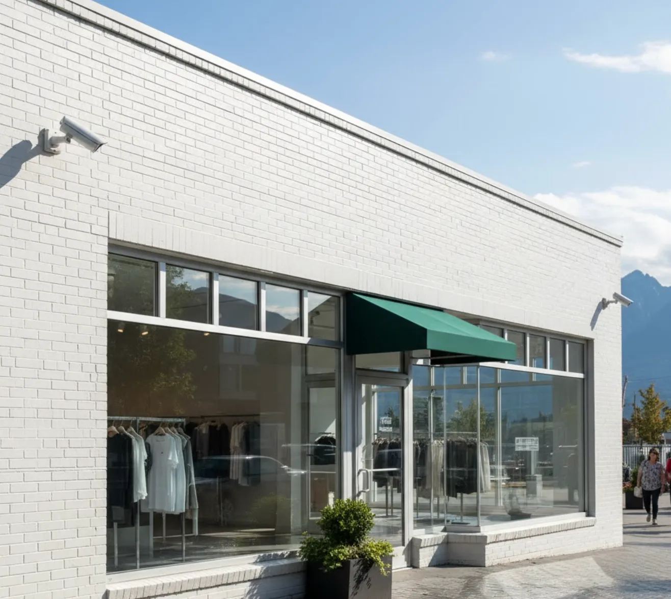 White brick clothing store with large windows displaying garments and a green awning above the entrance.