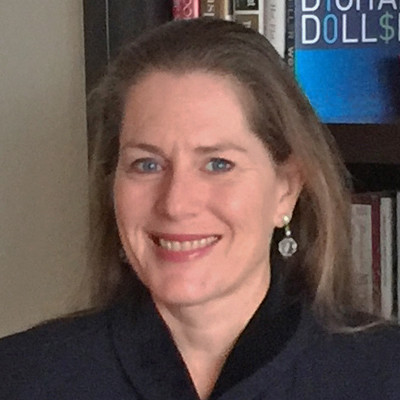 Smiling woman with light brown hair wearing earrings and a dark top, standing in front of a bookshelf.