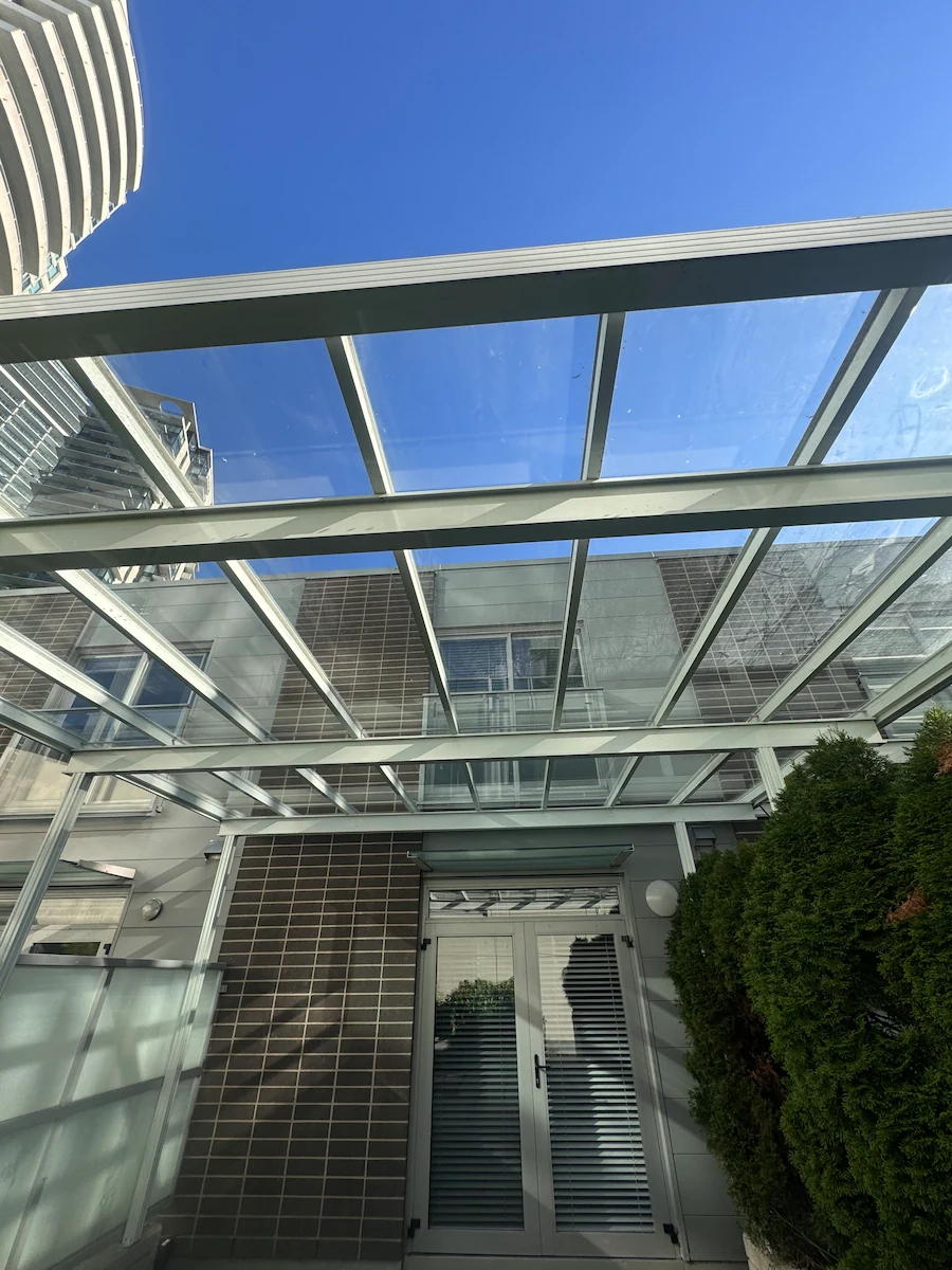 Glass awning after professional cleaning, restored to clear, transparent panels allowing full light through on a Vancouver property.