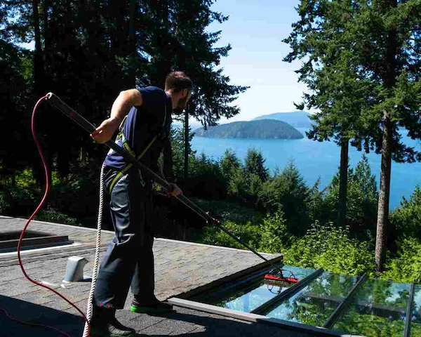 Technician cleaning glass awning with extension brush at residential property overlooking ocean view.