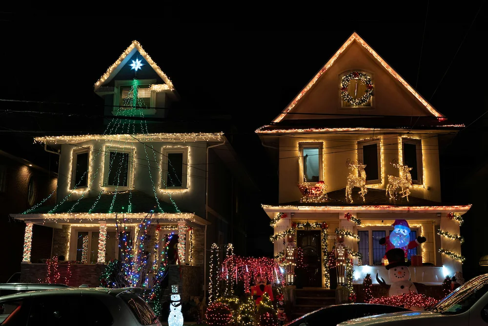 Two multi-story homes illuminated with colourful Christmas lights.