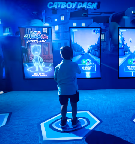 A little boi playing an augmented reality game in front of a digital screen, in the PJ Masks Hero City area in Planet Playskool.