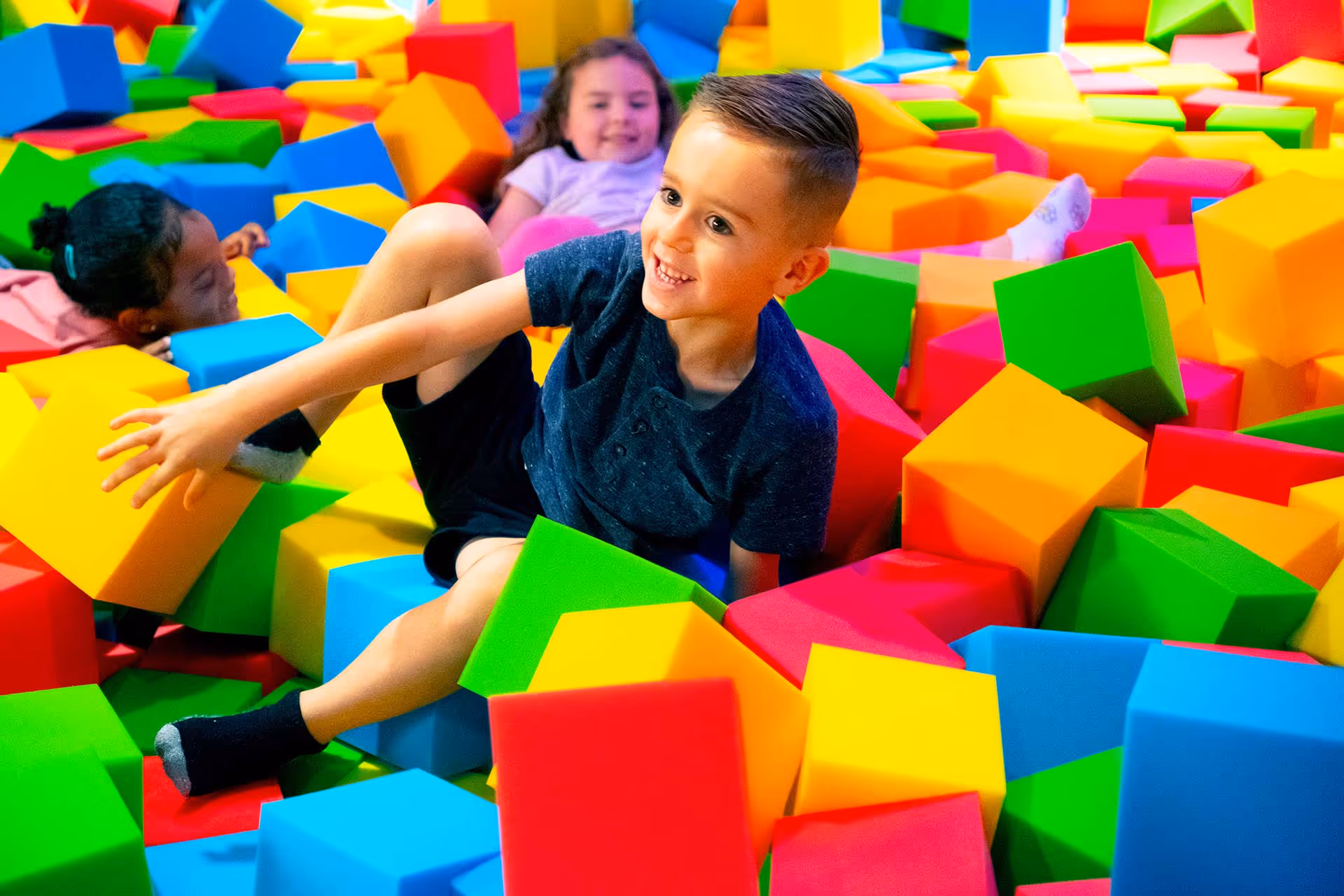 Kids playing in a colorful foam cube pit.