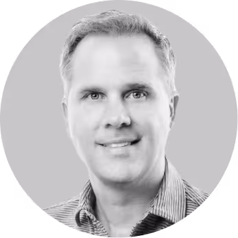 Black and white portrait of a middle-aged man smiling, wearing a striped collared shirt.