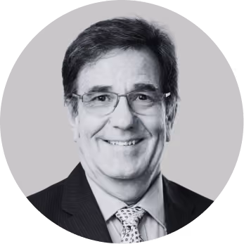 Smiling middle-aged man with glasses wearing a suit and patterned tie, black and white photo.