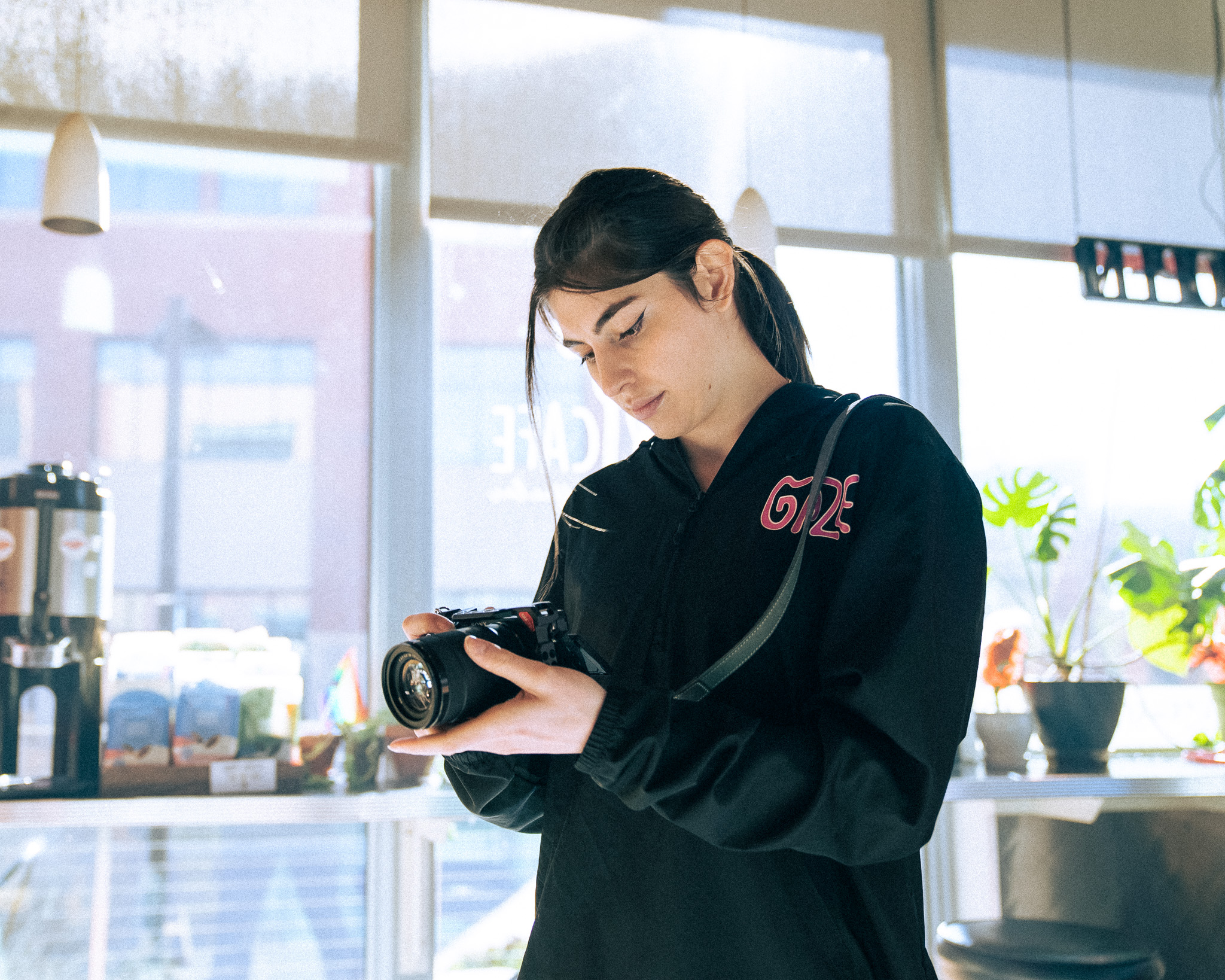 A picture of a woman in a gaze marketing hoodie with a camera focusing on taking a picture of something out of the images frame.