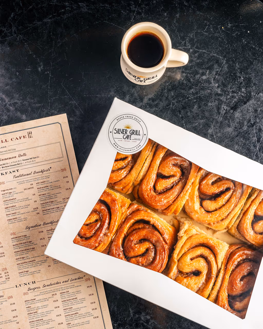 A box of cinnamon rolls on a table with some coffee next to them.