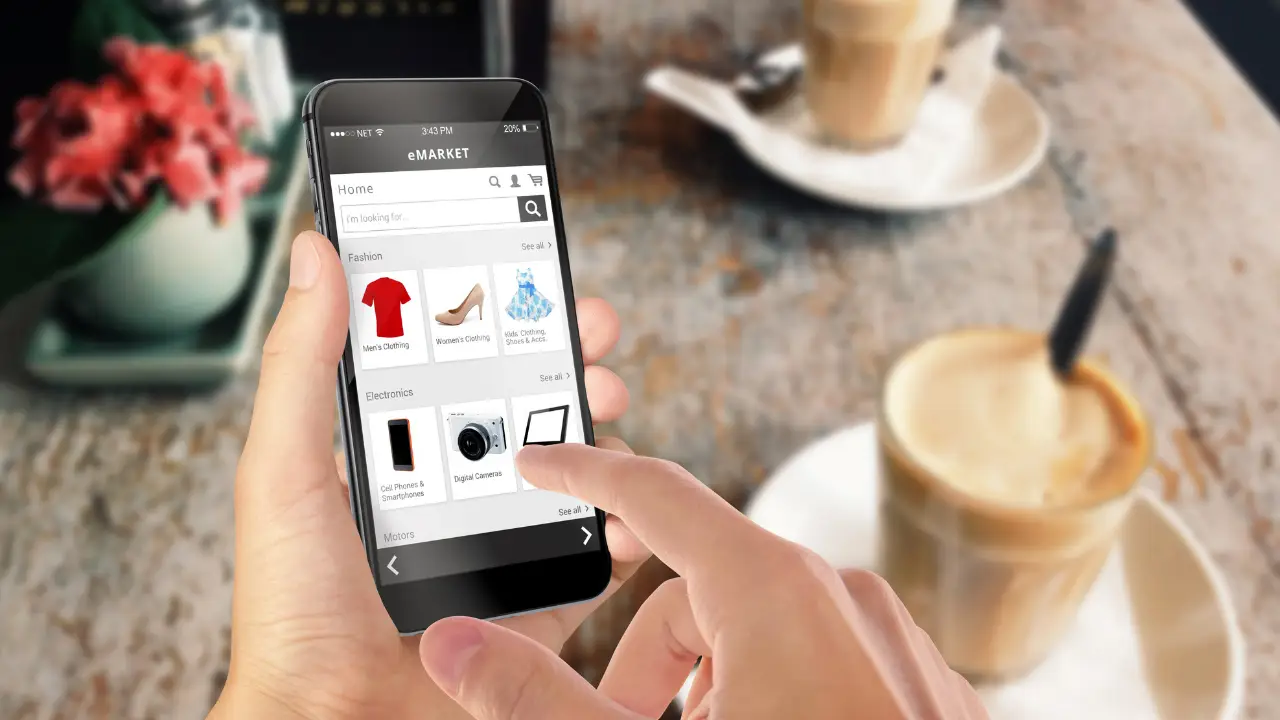 A person at a coffee table holding an mobile and browsing products on a webshop