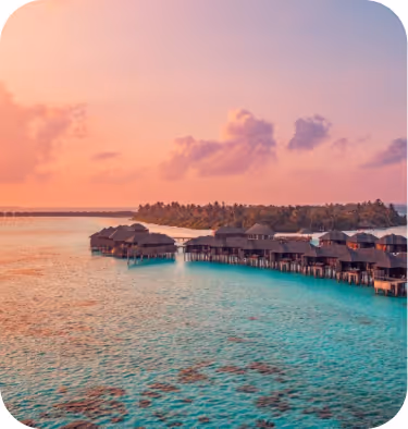 Overwater bungalows on a turquoise lagoon at sunset with a pink and purple sky.