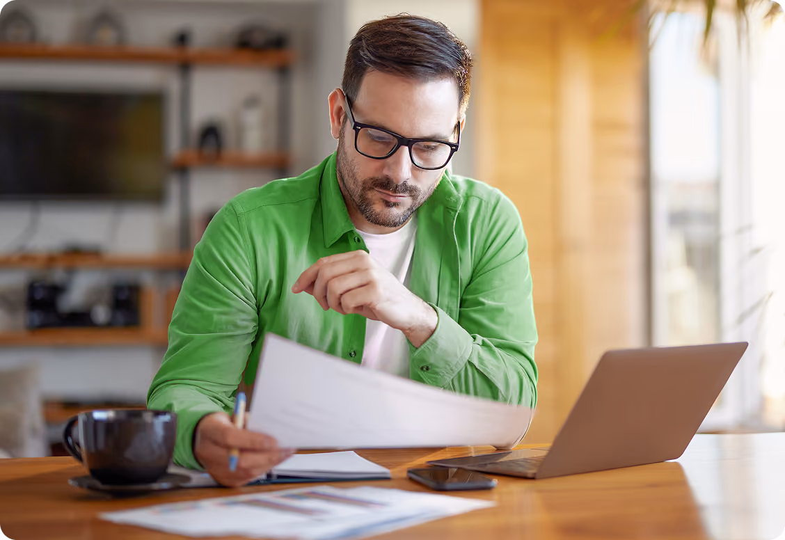 Man looking at a paper sitting at desk with laptop