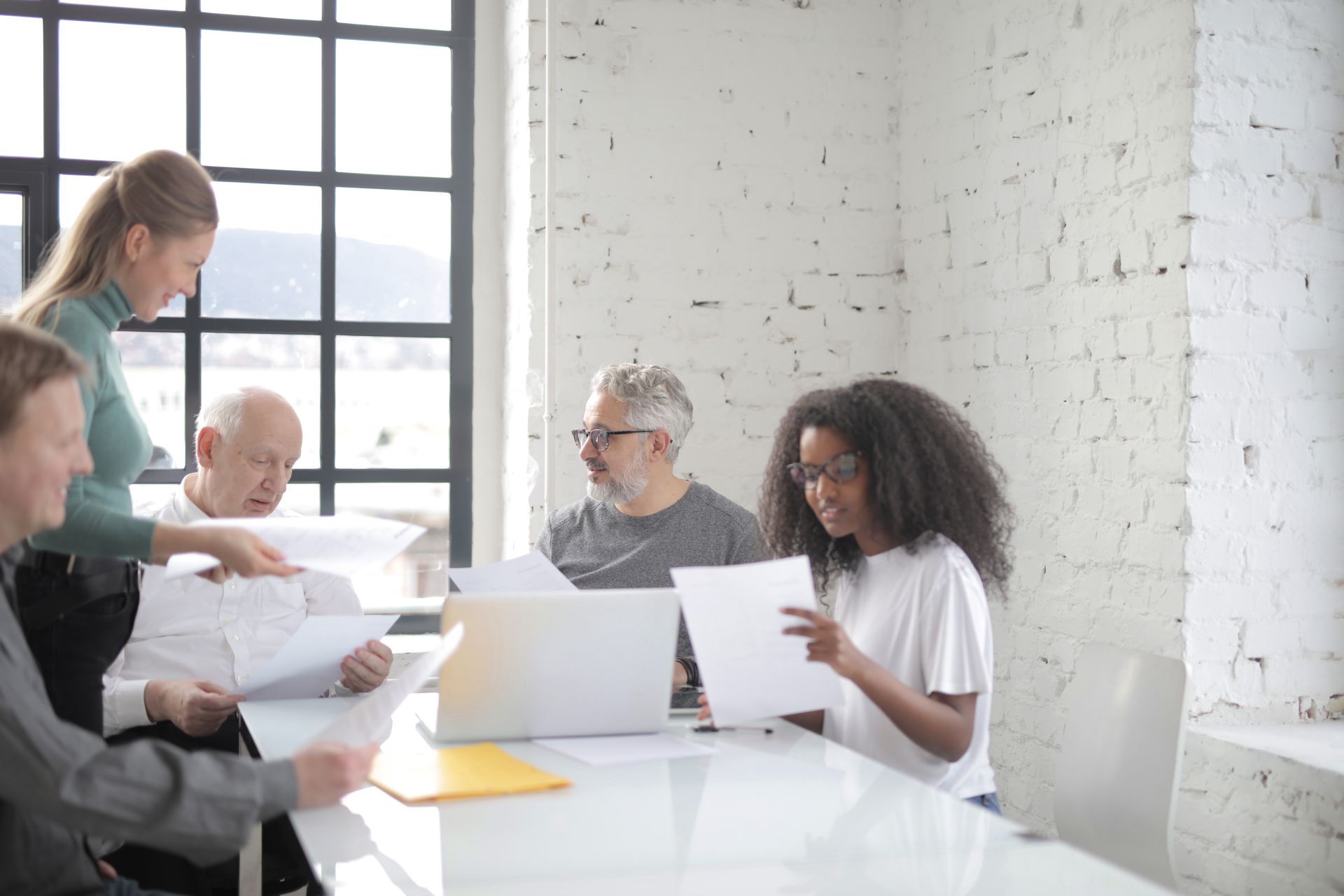 A small team reviewing papers and a laptop at a shared table in a bright office.
