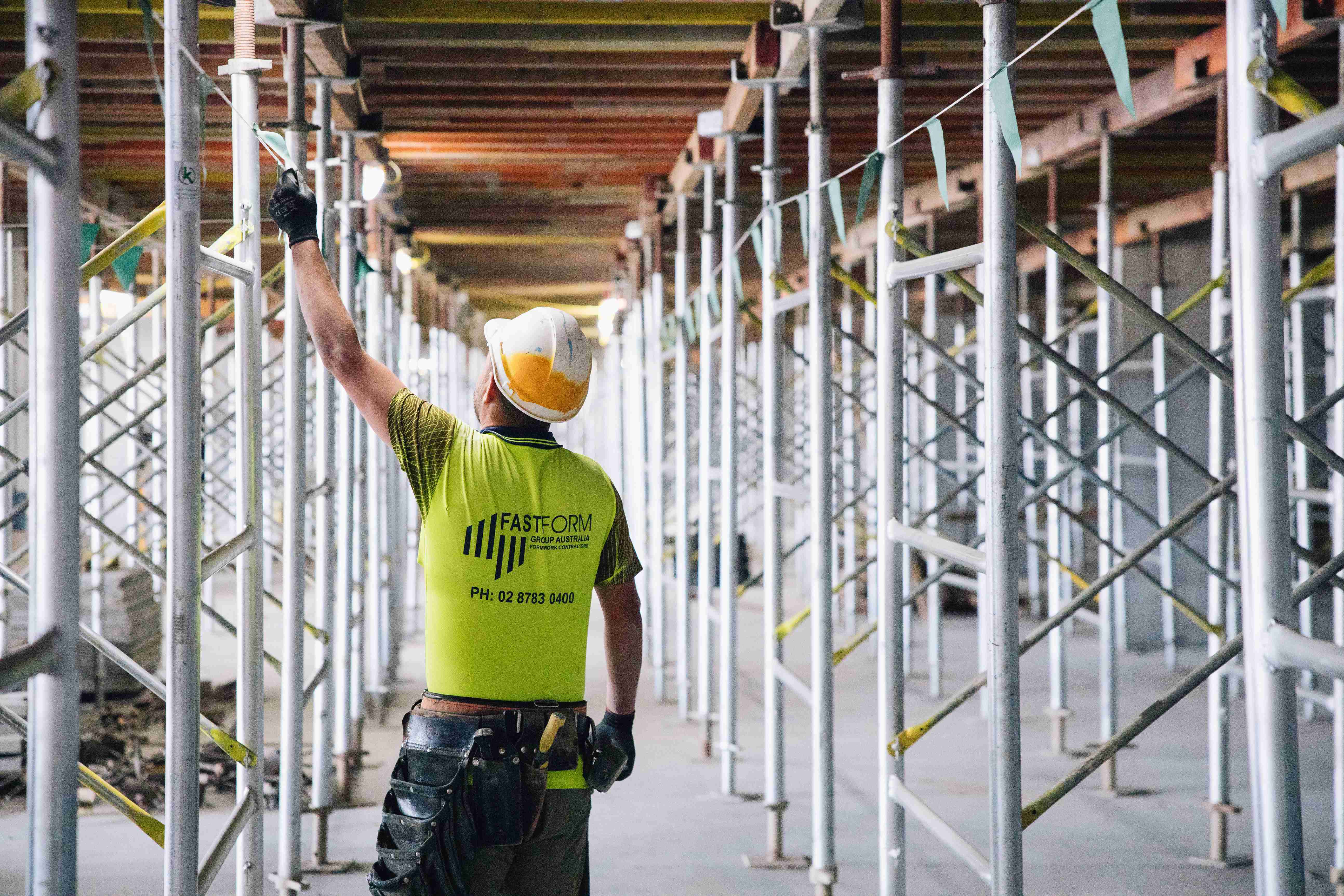 Construction worker carries lumber on shoulder near portable toilet; Fastform logo.