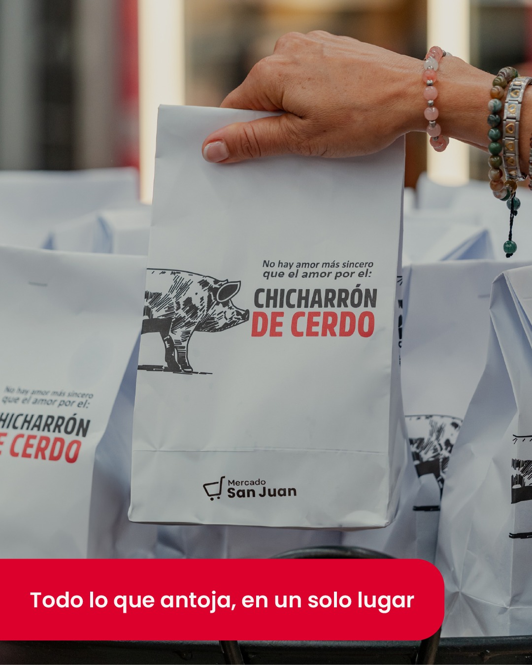 Mano sosteniendo una bolsa blanca con la frase "No hay amor más sincero que el amor por el chicharrón de cerdo" y un dibujo de cerdo, junto con bolsas similares de fondo.