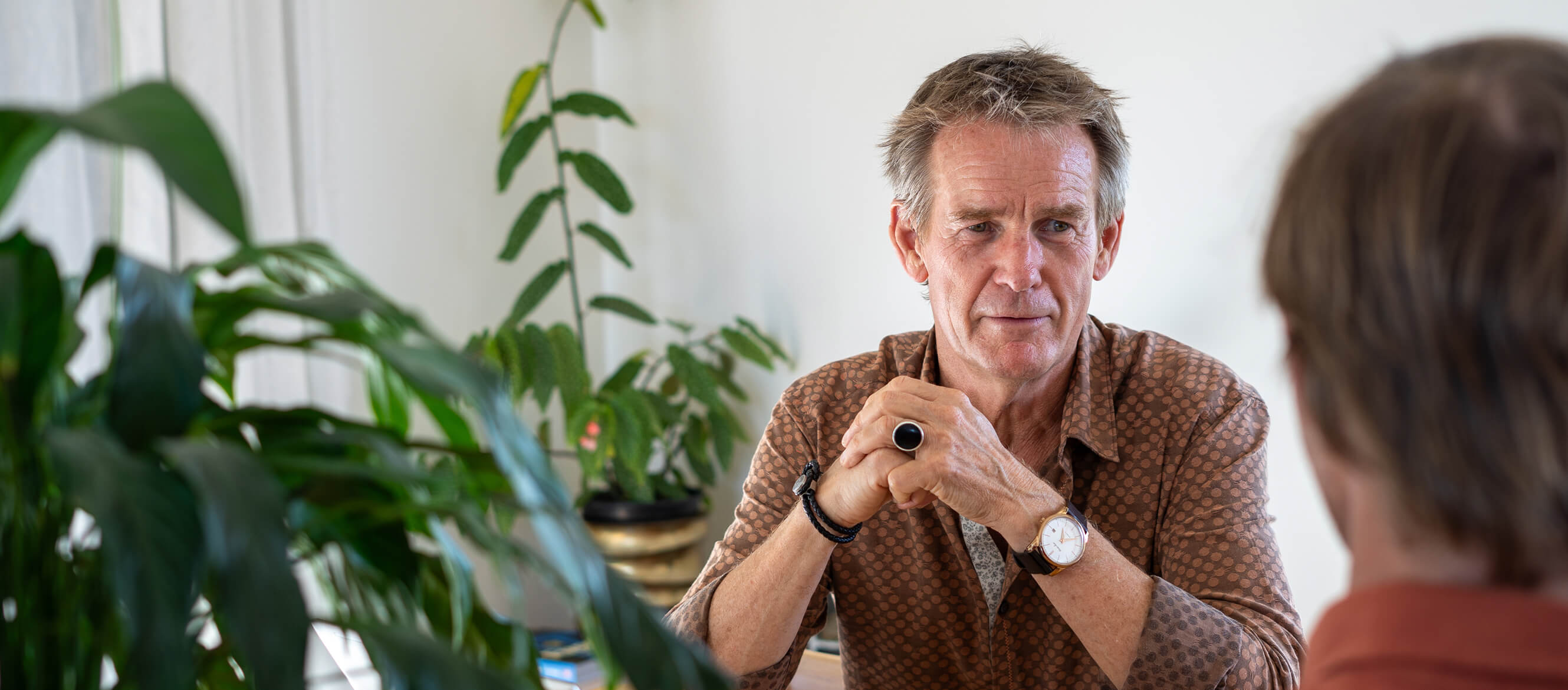John McConnell listening to a client in a meeting, with plants in the foreground.