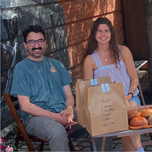 Co-owners of Baci's Bagel Co sitting at table smiling with spreak of bagels in front of them