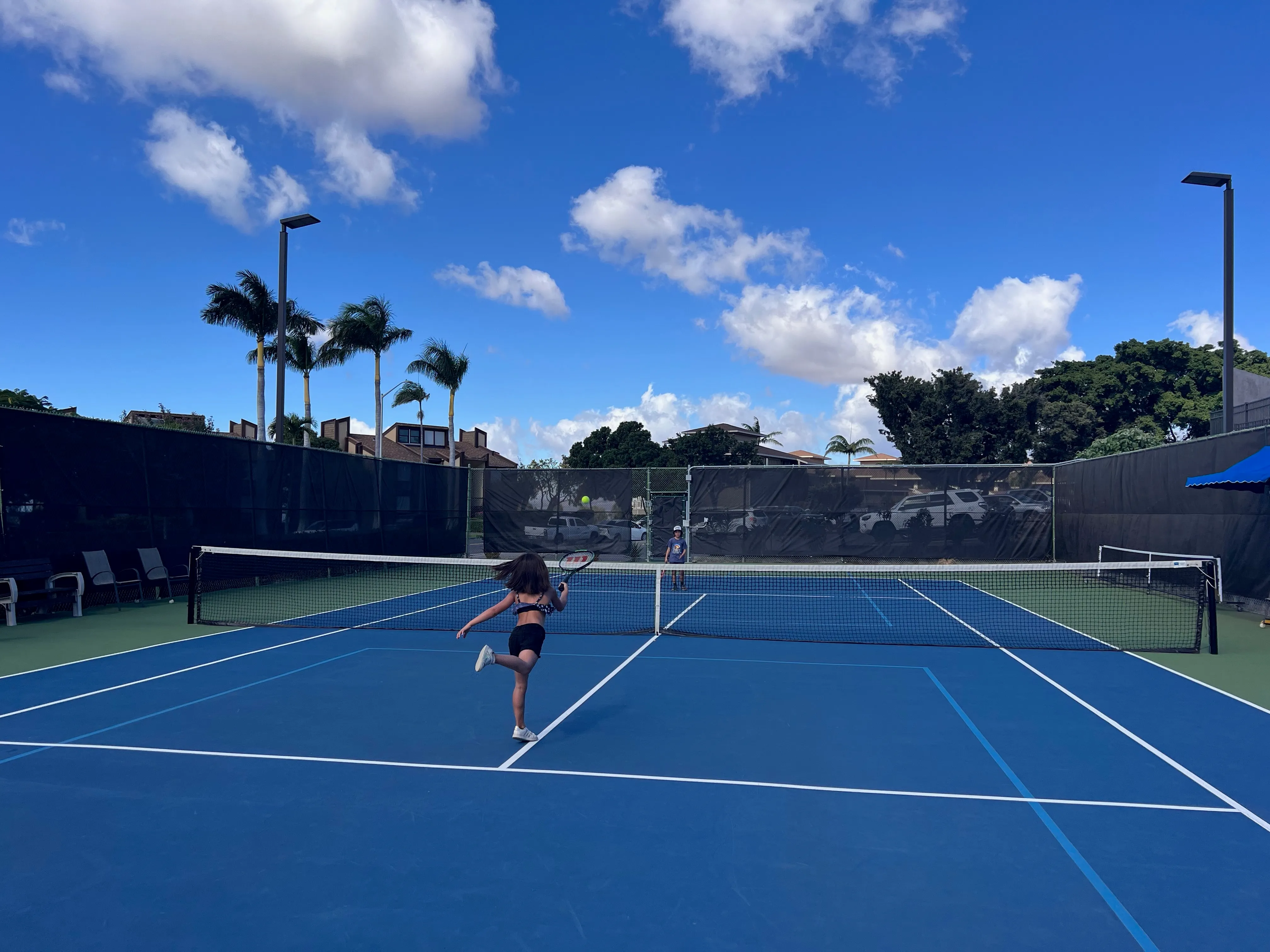 Playing on the Waikoloa Village tennis courts, palms and blue sky behind.