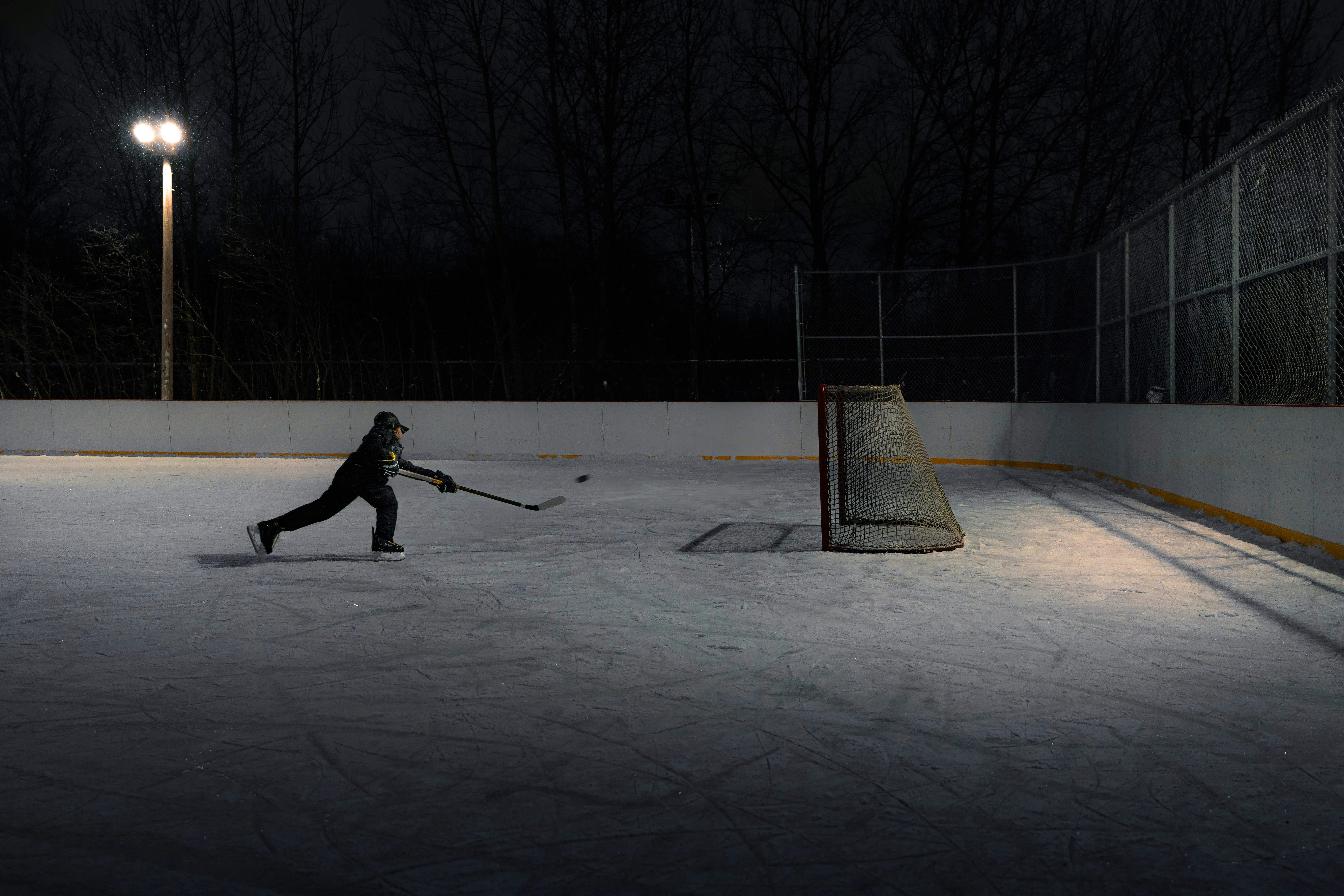 A young hockey player shoot a puck in a net at an outdoor skating rink