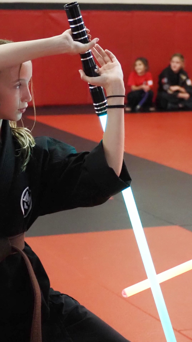 student practices a sword technique with a light-saber toy