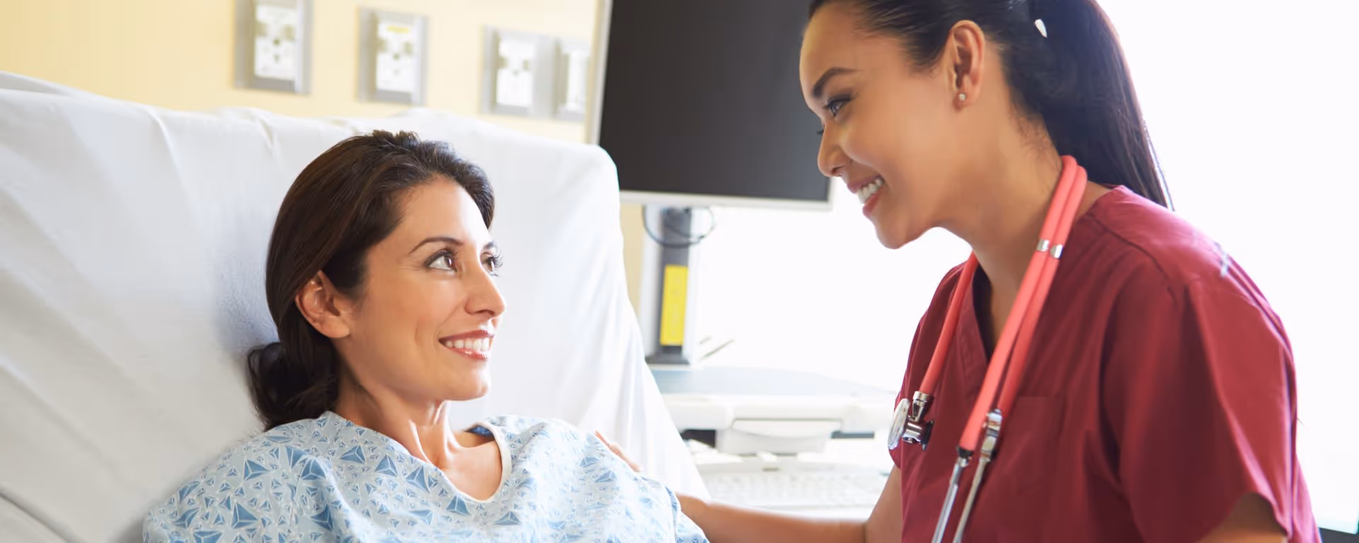 Woman in hospital bed smiling at nurse. 
