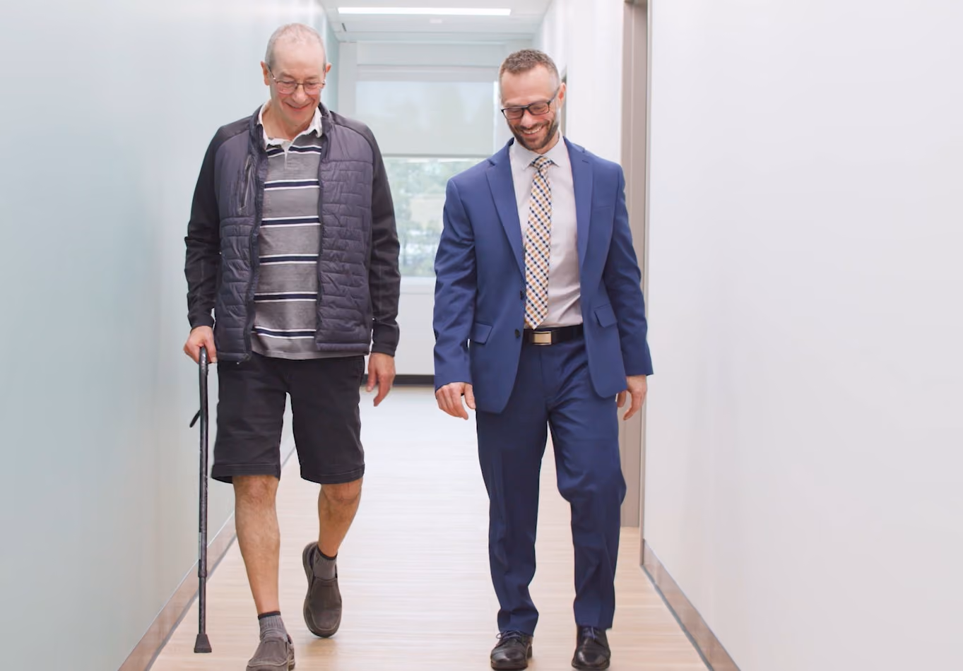 Gateway surgeon accompanying older patient with a cane down clinic's hall