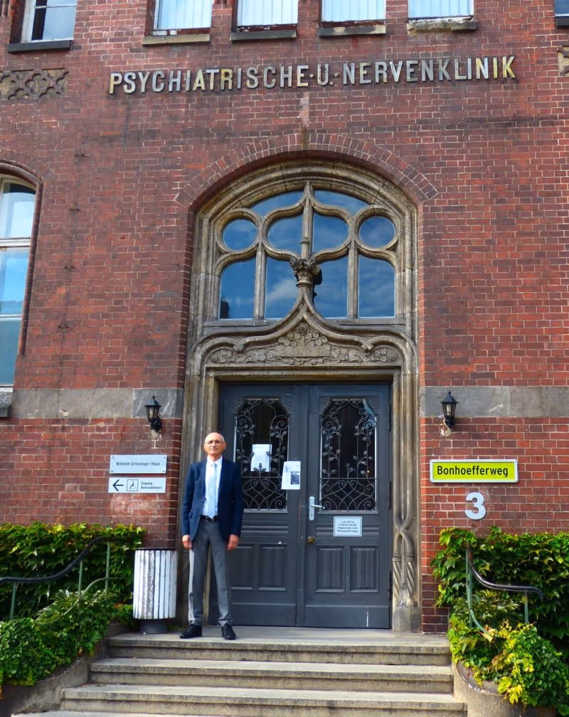 Dr. standing in front of the historic entrance to a psychiatric and neurology clinic in Germany.