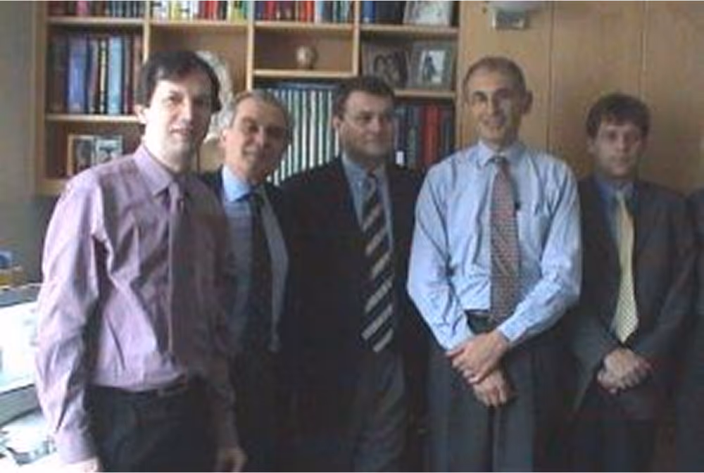 Group of five men in formal attire standing indoors, posing for a group photo.