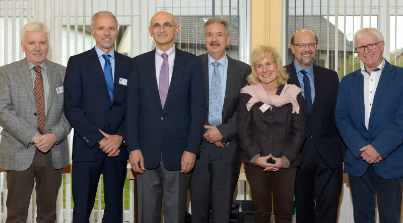 Group of seven people in business attire standing together for a formal group photo, with one woman in the group.