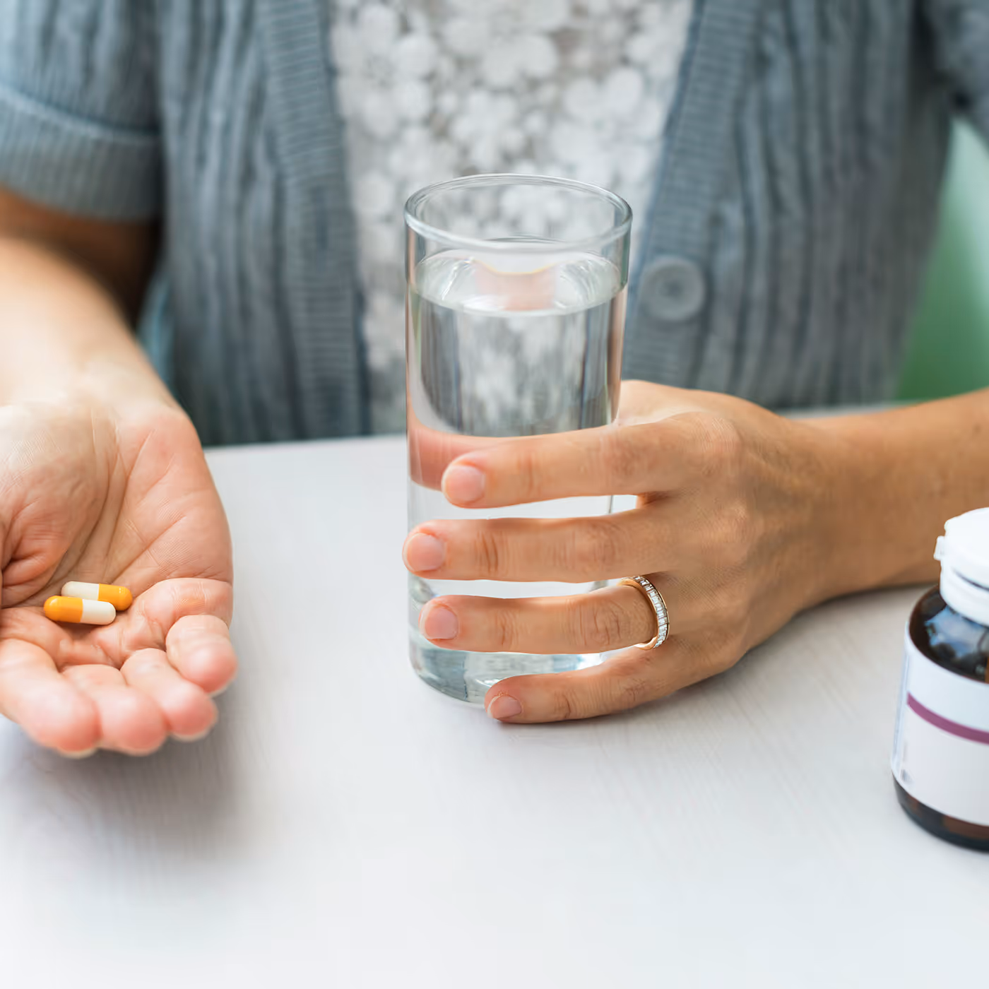 Patient holding migraine medication pills and glass of water.