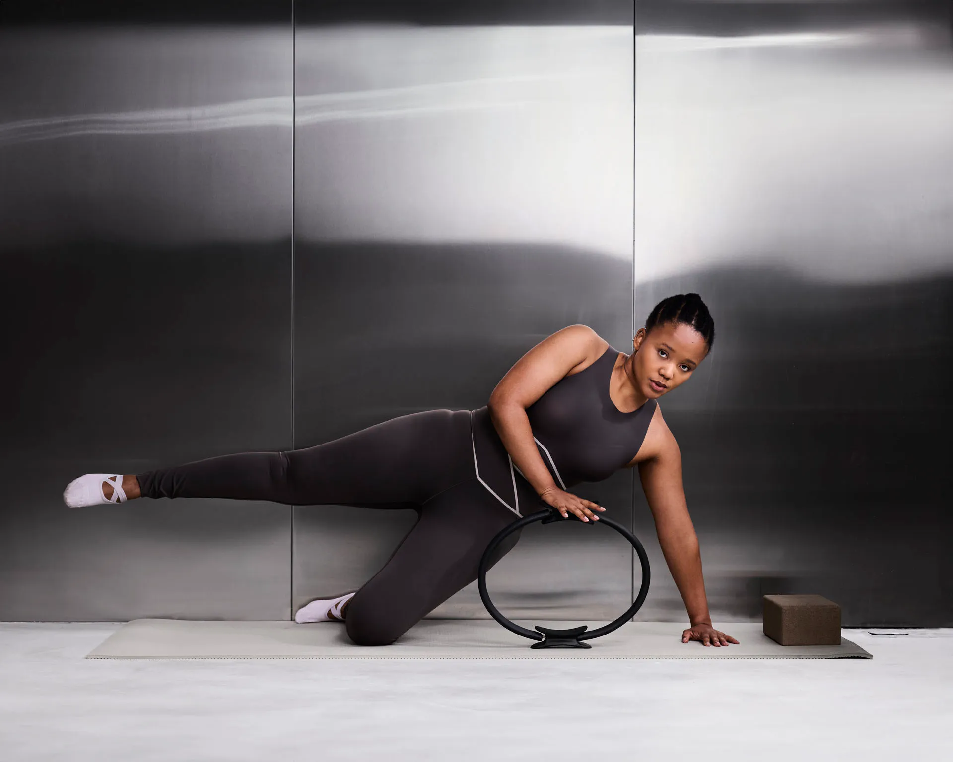 Woman in black workout clothes doing side leg raises with a Pilates ring on a mat indoors.