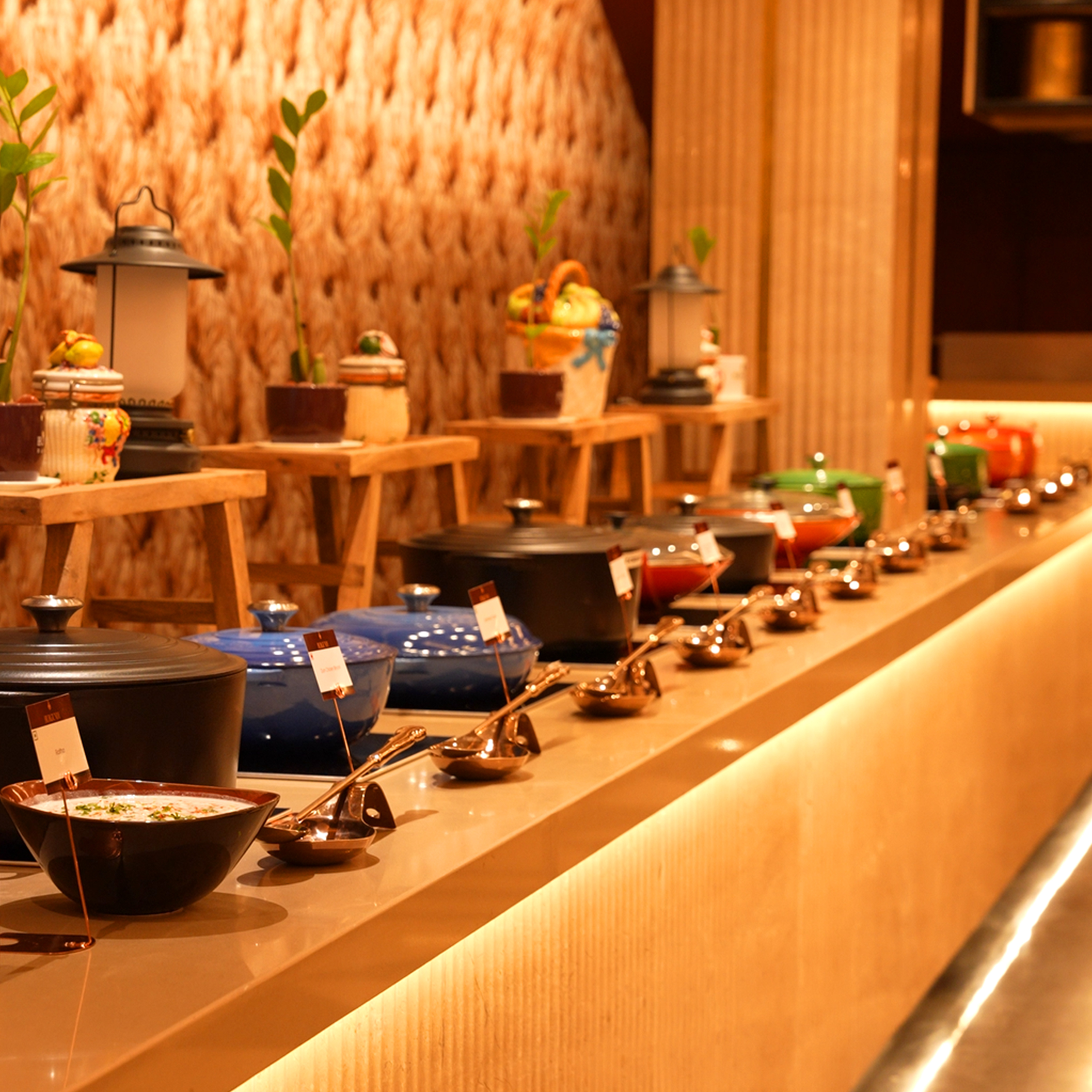 Buffet line with covered serving dishes and ladles arranged on a lit countertop.