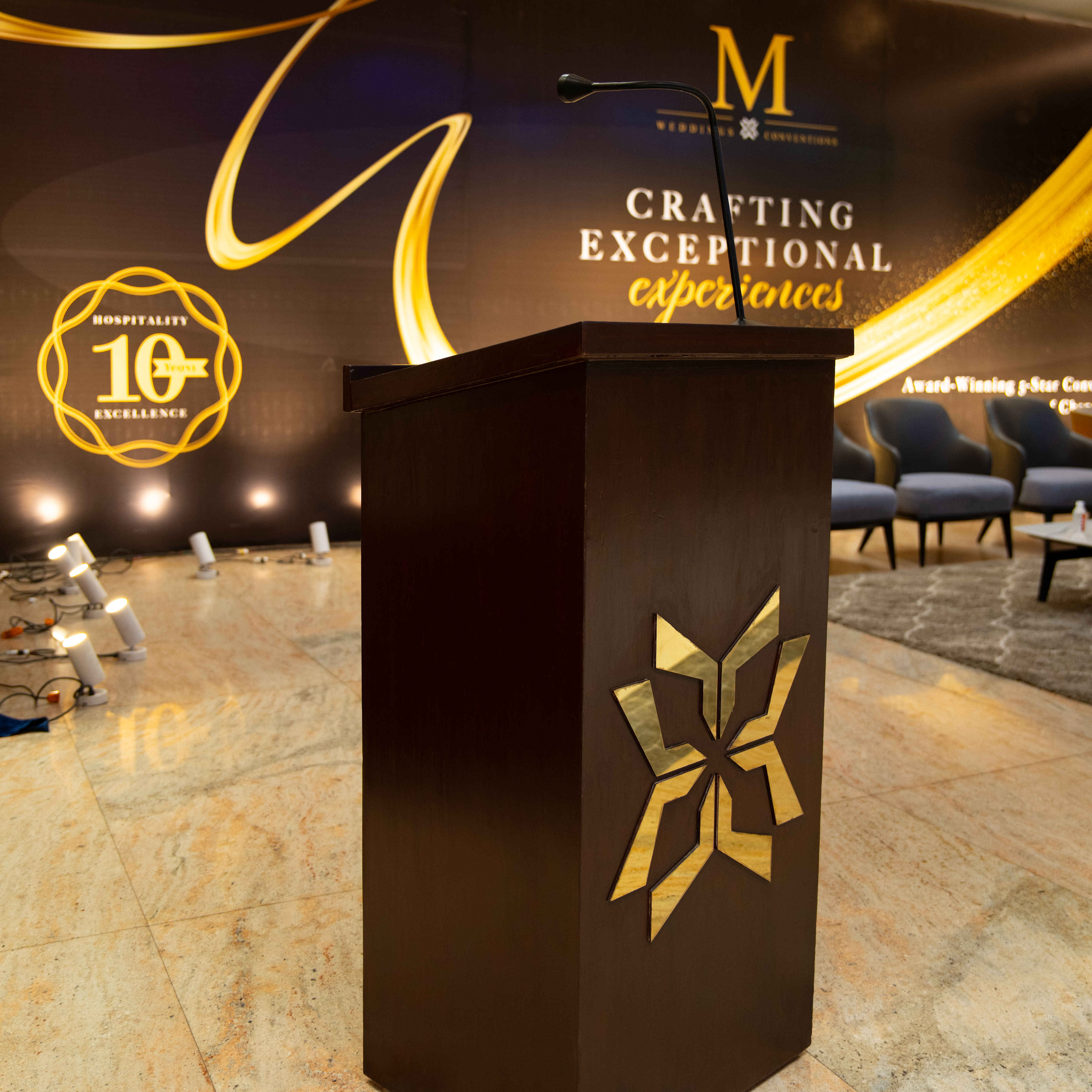 Wooden podium with a golden star emblem and a microphone in front of a backdrop reading 'Crafting Exceptional Experiences' and 'Hospitality 10 Years Excellence'.