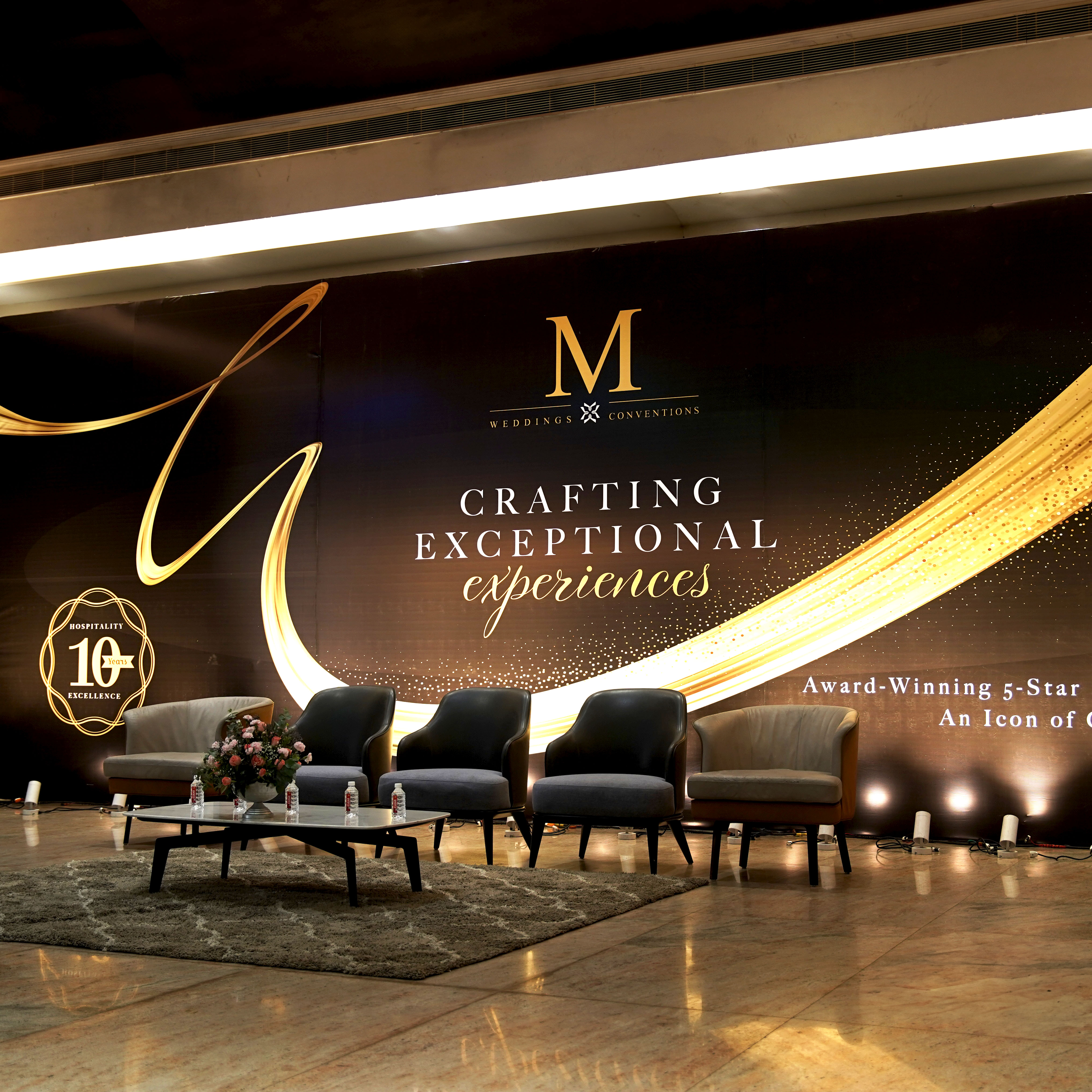 Lobby area with five chairs arranged in a row behind a table with flower arrangement, set against a backdrop with the text 'Crafting Exceptional Experiences' and 'Award-Winning 5-Star'.
